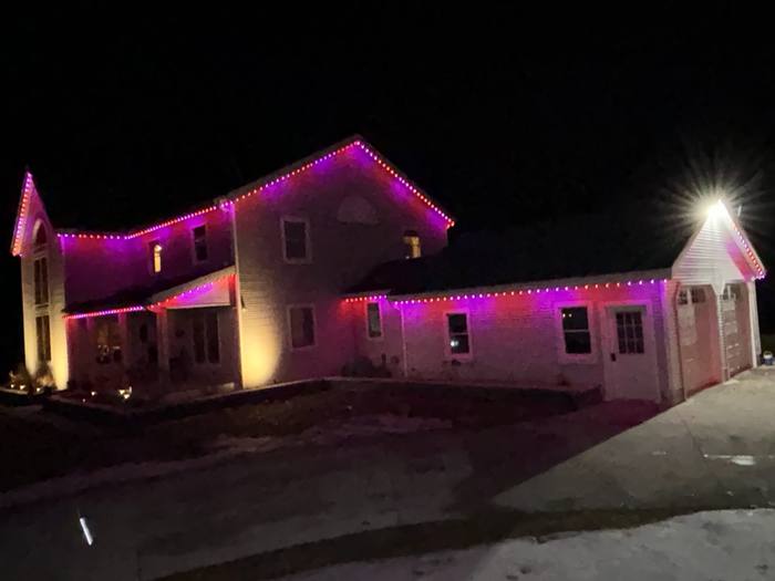 Large home with purple and red Trimlight along the roofline at night