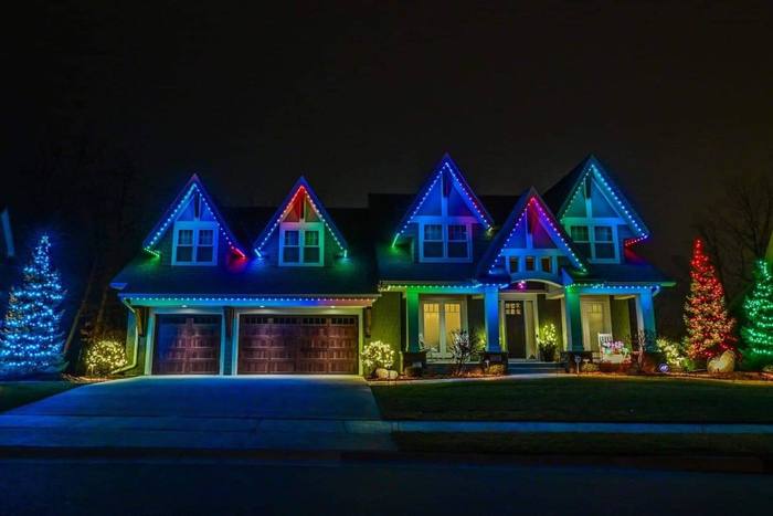 Home with blue, green, purple, and red Trimlight beside lit evergreen trees