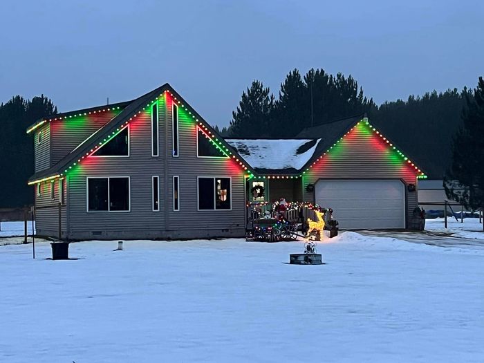 Snow-covered A-frame home with red and green Trimlight outlining the gable and windows