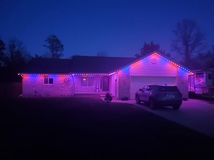 Ranch home with purple and blue Trimlight roofline lighting at dusk
