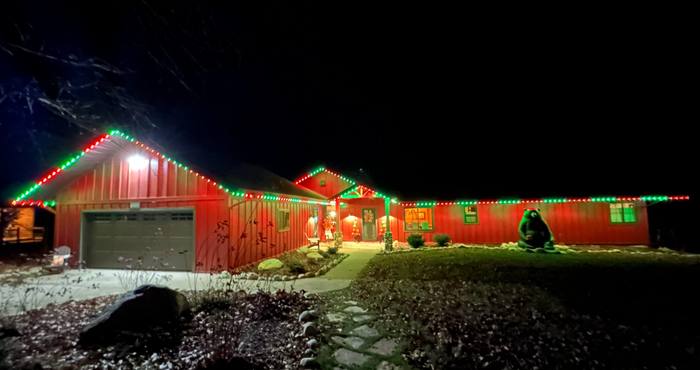 Red barn-style home with green and red Trimlight and holiday yard decor