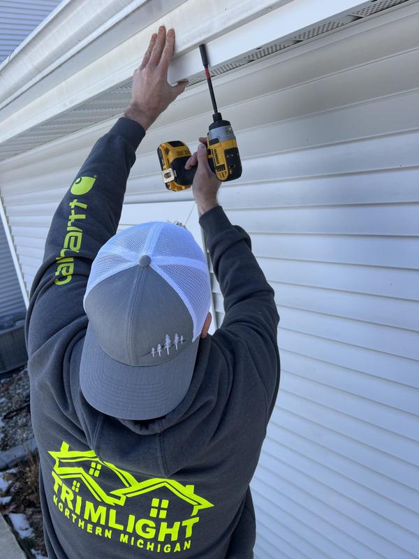 Installer securing Trimlight channel to a roofline with a drill